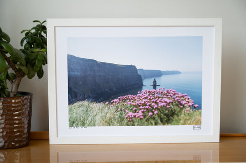 Iconic Cliffs of Moher photograph with sea pink wildflowers in the foreground, professionally presented in a bright white frame for a luxury Irish gift.