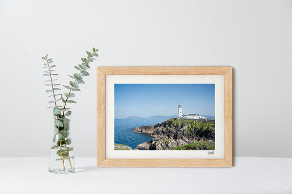 Fanad Lighthouse photograph in a natural wood frame showing Donegal coastline under a clear blue sky